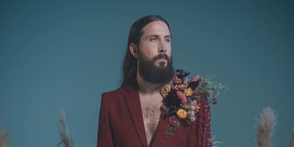 Avi Kaplan in red suit sitting in a desert