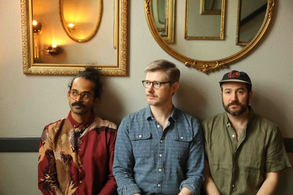 3 members of Darlingside standing in front of a wall with mirrors
