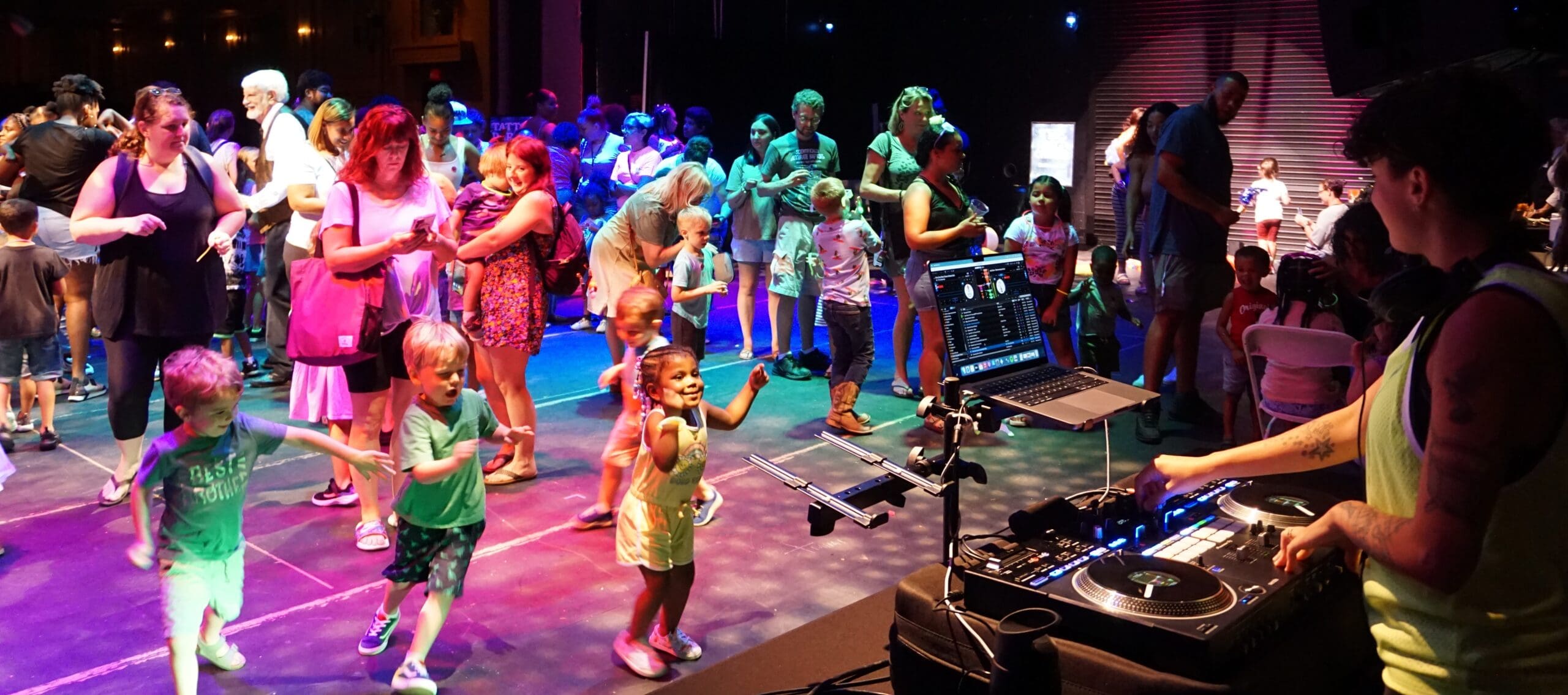 Children of all ages dancing on the stage with a DJ playing music