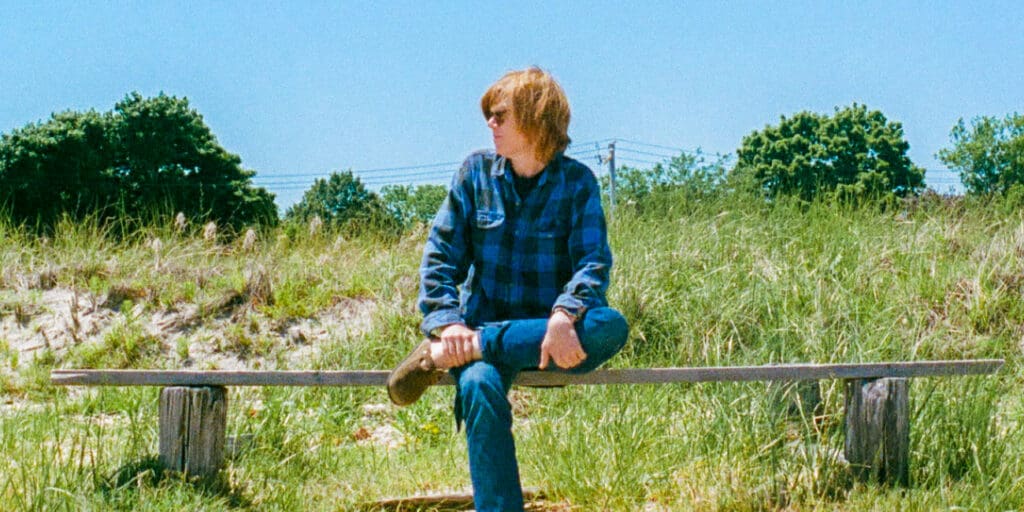 Brett Dennen sitting on a bench in a green field