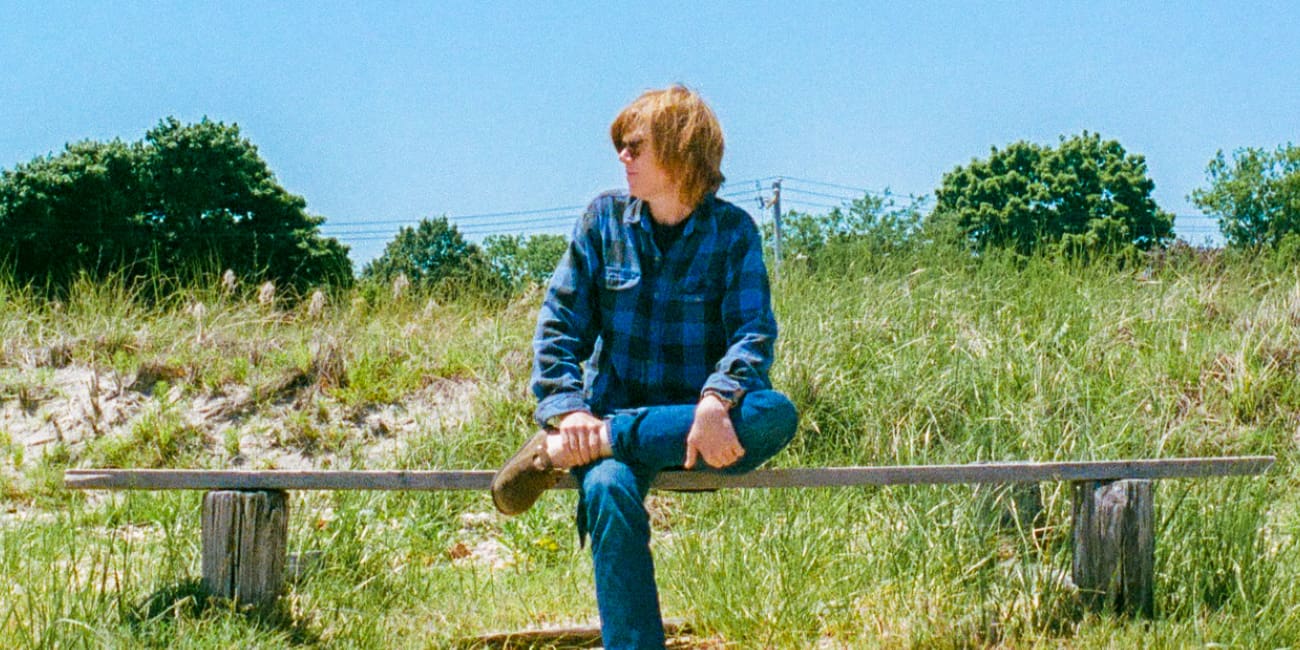 Brett Dennen sitting on a bench in a green field