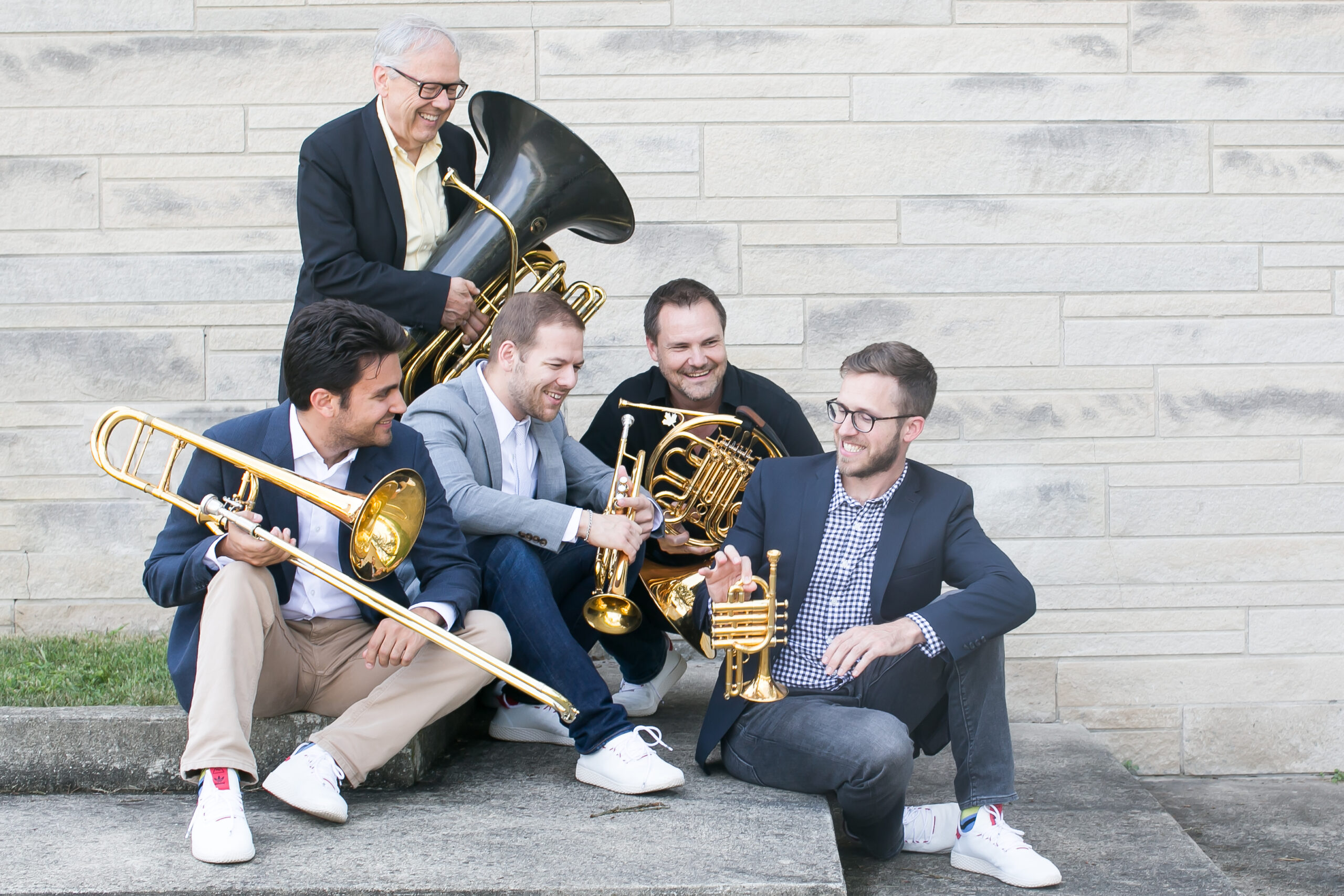 photo of the five members of Canadian Brass sitting on a stair and laughing