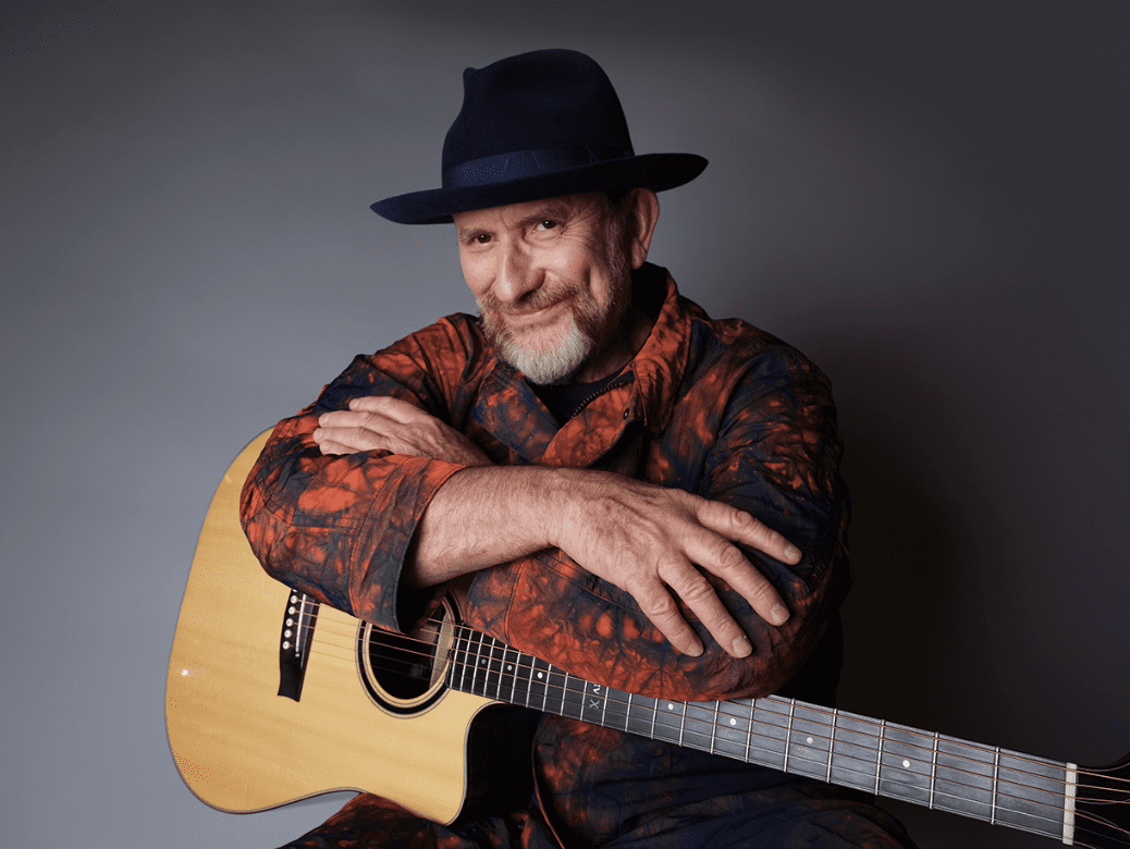 Colin Hy leaning over an acoustic guitar wering dark fedora