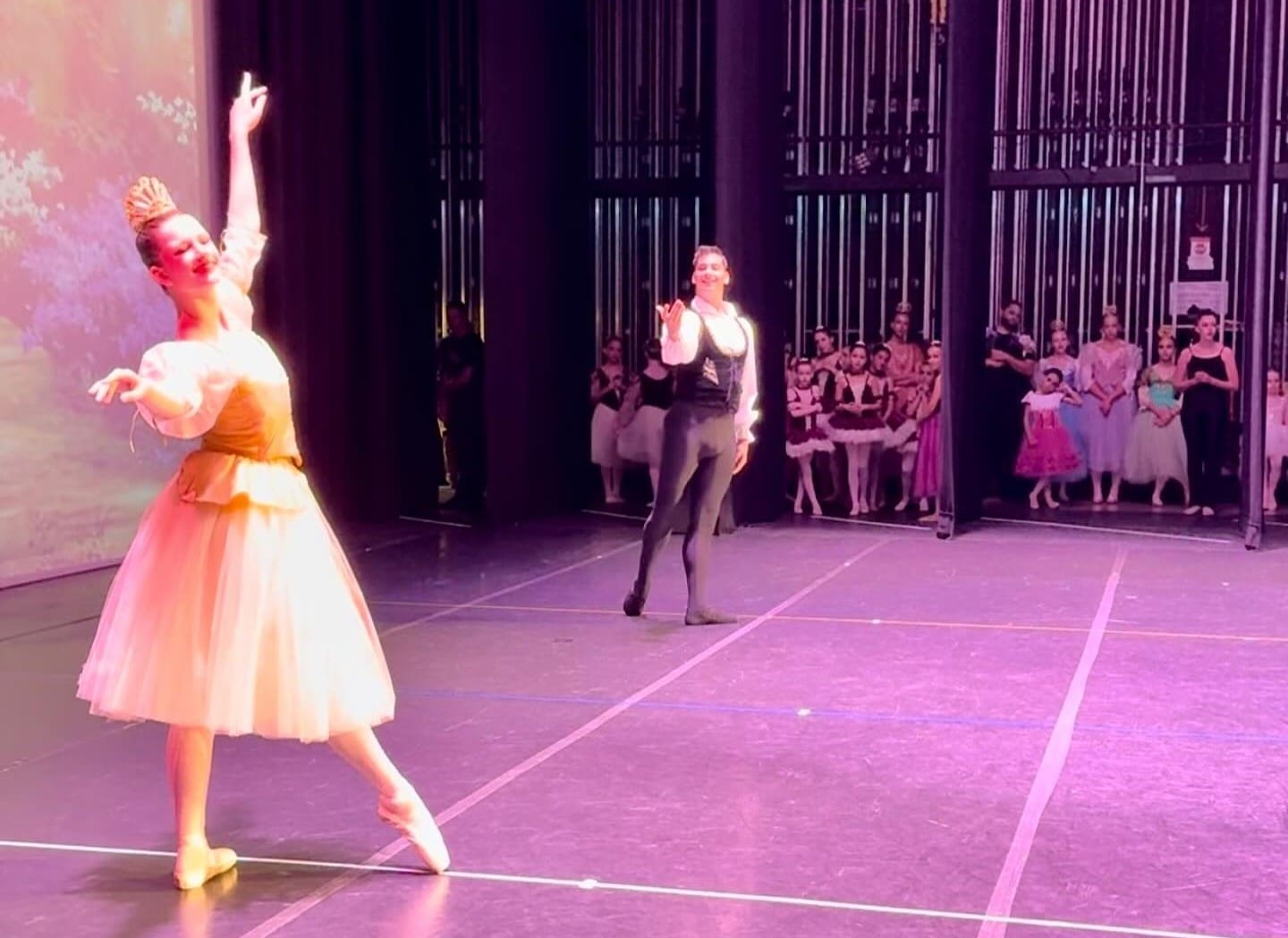 Dance It Forward featured ballet dancer on the left with male dancer facing her an youth dancers in the background in the wings