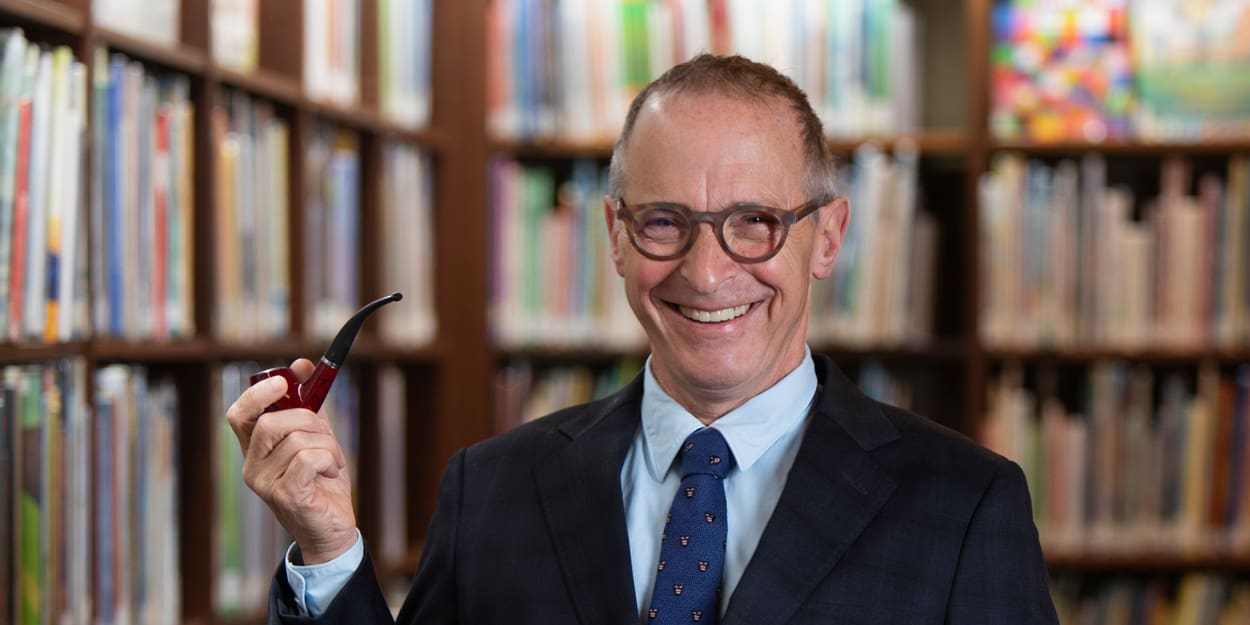 American author, humorist, comedian, and radio contributor David Sedaris standing in a library stack smiling