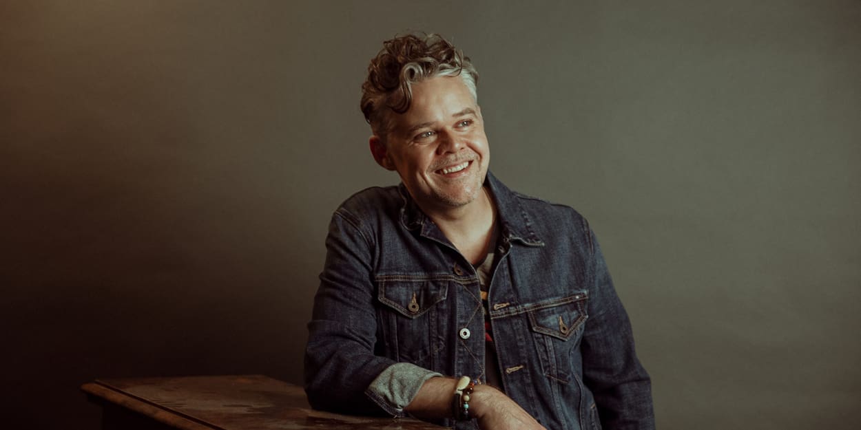 Portrait of Gabe Dixon leaning on a piano against an earth tone background