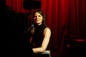 Lindsey Kraft sitting at the piano with red curtain behind