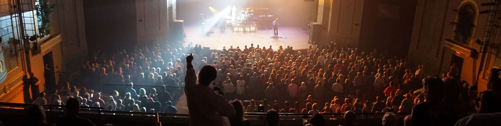 Image of the audience in the Strand Theatre standing at their seats as a rock-n-roll band plays on stage.