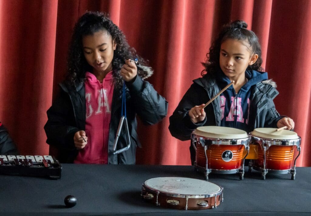 Two young children play percussion instruments