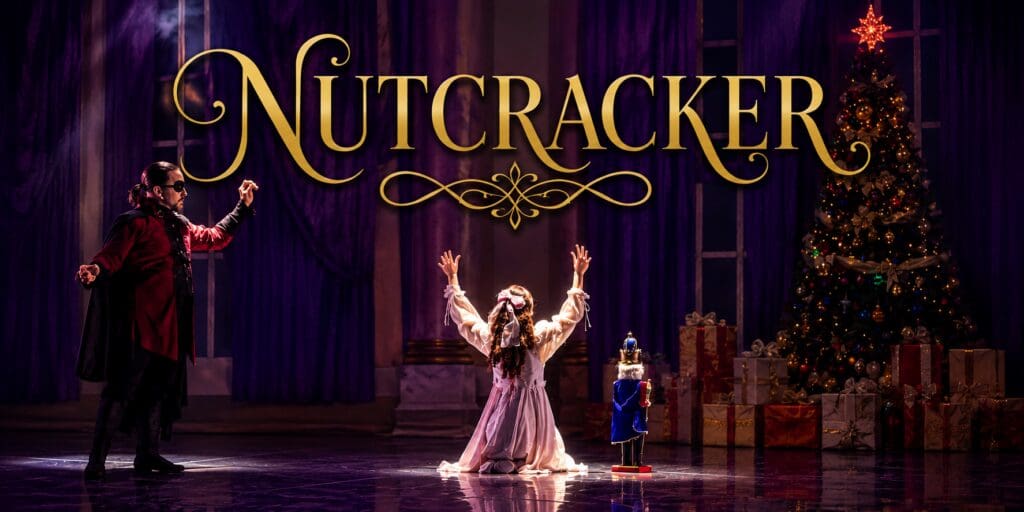 scene from The Nutcracker with Clara on her knees in front of the Christmas tree with a nutcracker next to her and Drosselmeyer to her left