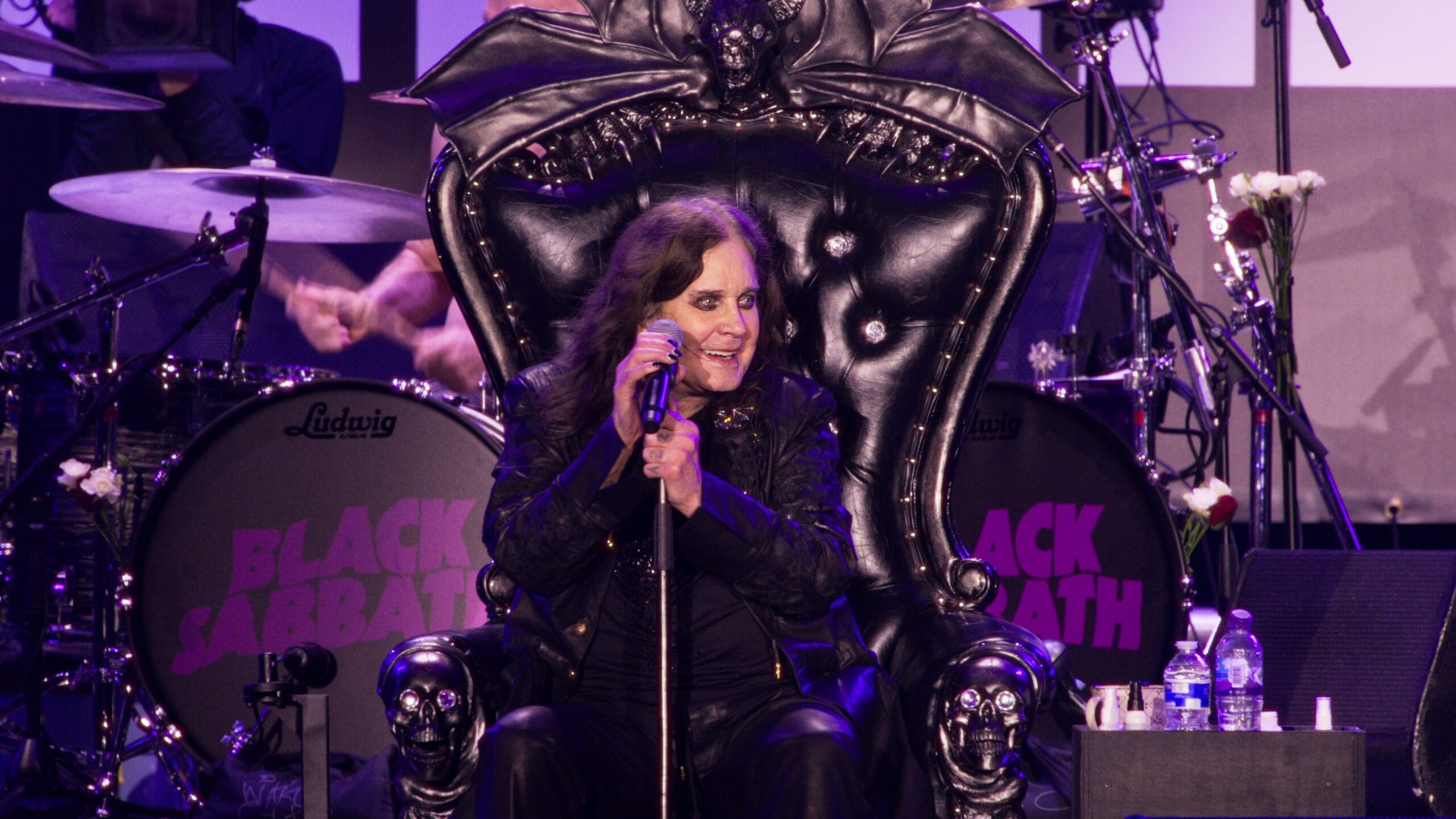 Flm still of Ozzy Osbourne on stage seated in his black leather "throne" with a microphone