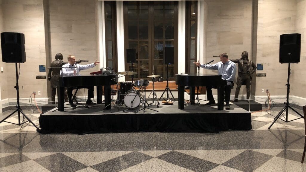 2 Pianists at dueling pianos on either side of the stage, pointing to the other