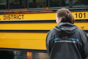 Appell Center staff member greets a school bus filled with kids before a show