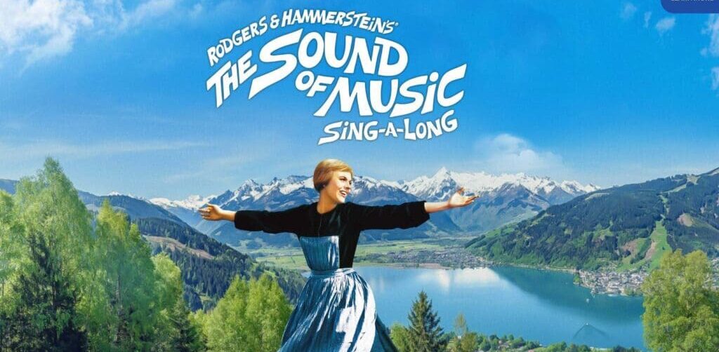 Movie image of Julie Andrews at the top of the mountain with arms outstretched and the film title above in the blue sky