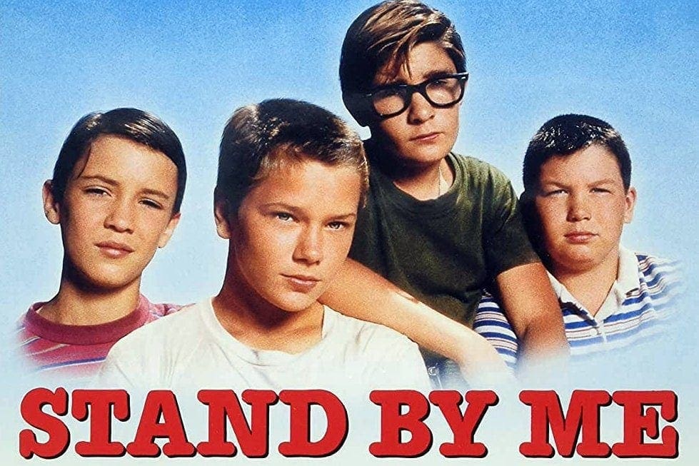 The main characters of Stand By Me in a group looking into the camera on a blue gradient background