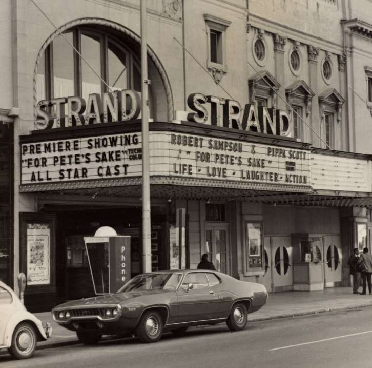 Old black and white photograph of the exterior of the Strand Theatre. The marquis reads, "Premiere Showing 'For Pete's Sake' technicolor, All Star Cast; Robert Sampson & Pippa Scott, 'For Pete's Sake' technicolor, Life - Love - Laughter - Action."