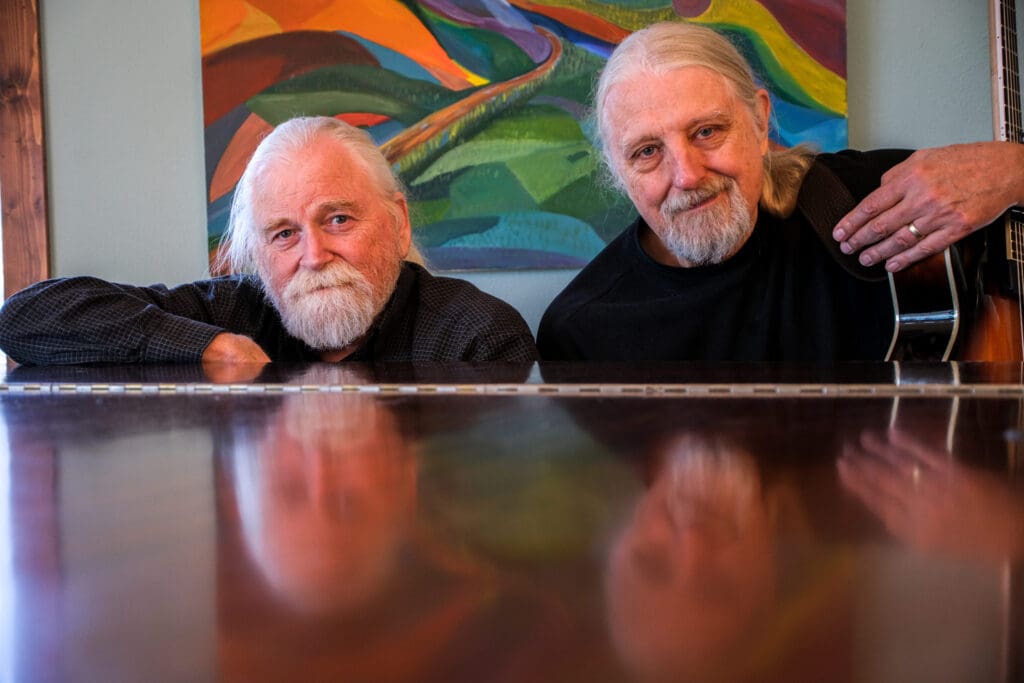 Two men who are Trout Fishing in America sitting at the piano, one holding a guitar