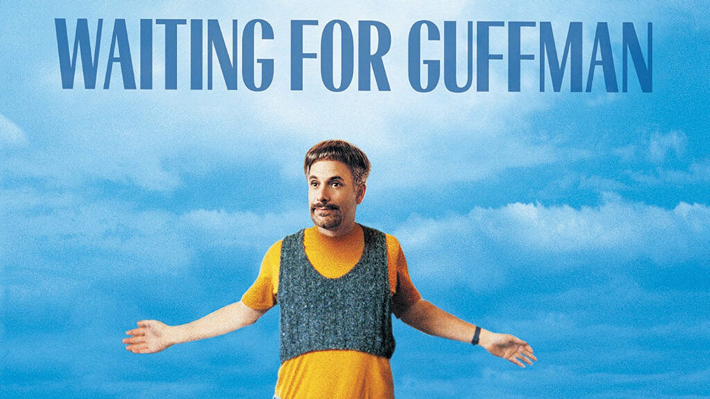 A man standing against a blue sky with his arms outstretched and the words Waiting for Guffman above him.
