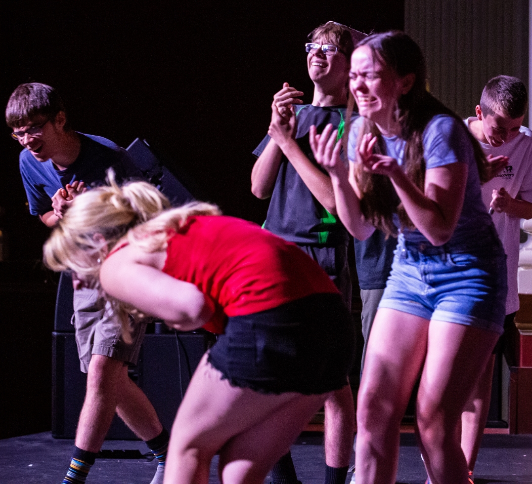Teenagers double over with laughter on stage.