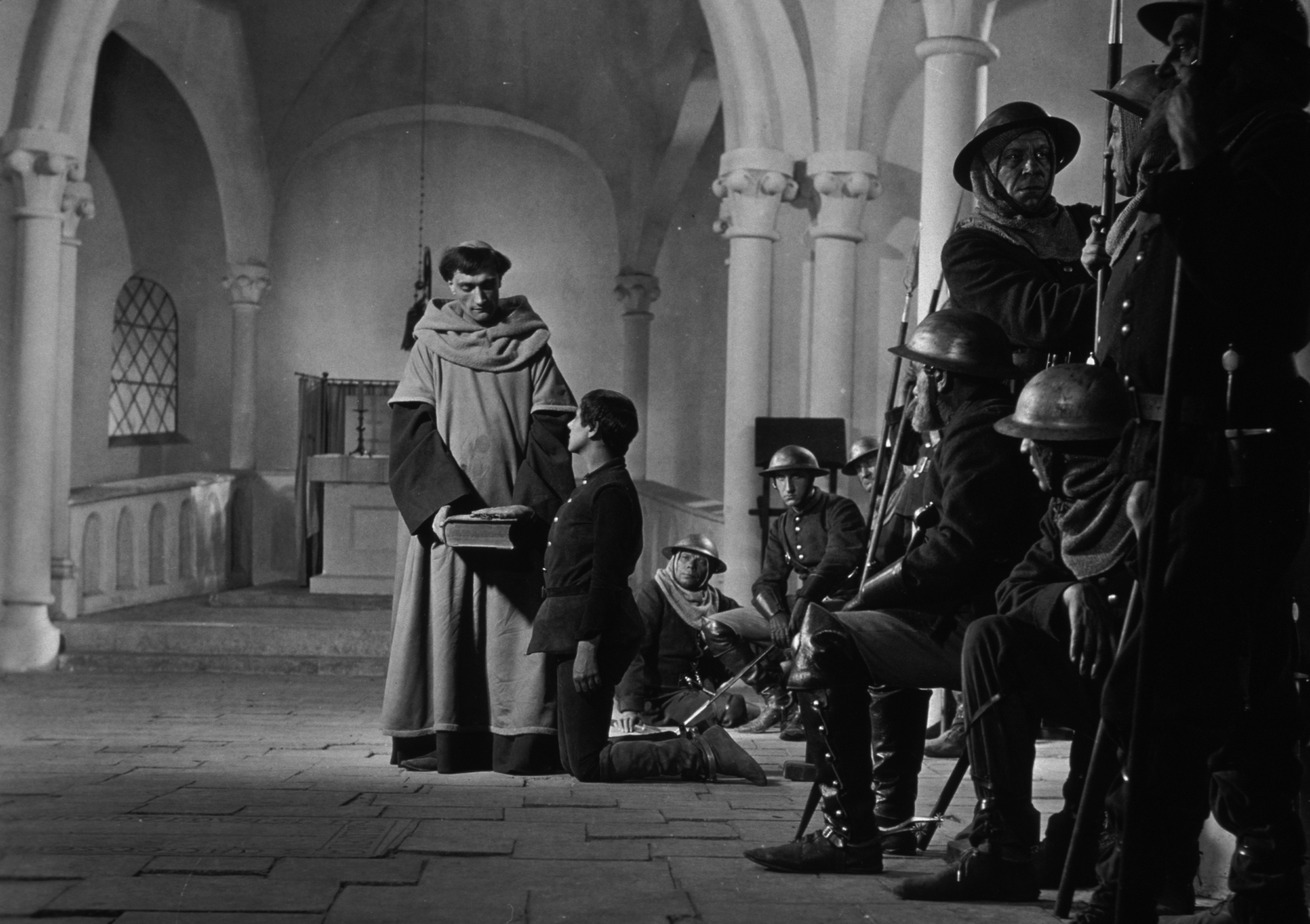 b/w image of Joan of Arc kneeling by a priest