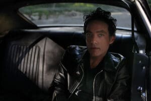 Jakob Dylan wearing a black leather jacket sitting in the back seat of a car